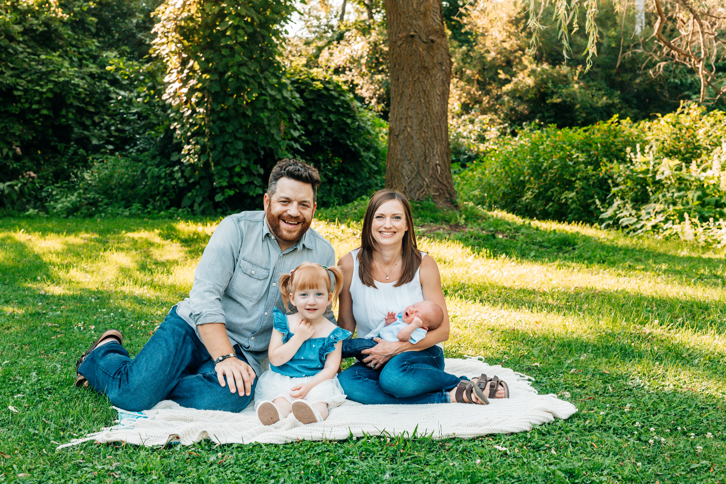 family with newborn sitting outside under a willow tree for an outdoor newborn session with Chelsey Kae Photography