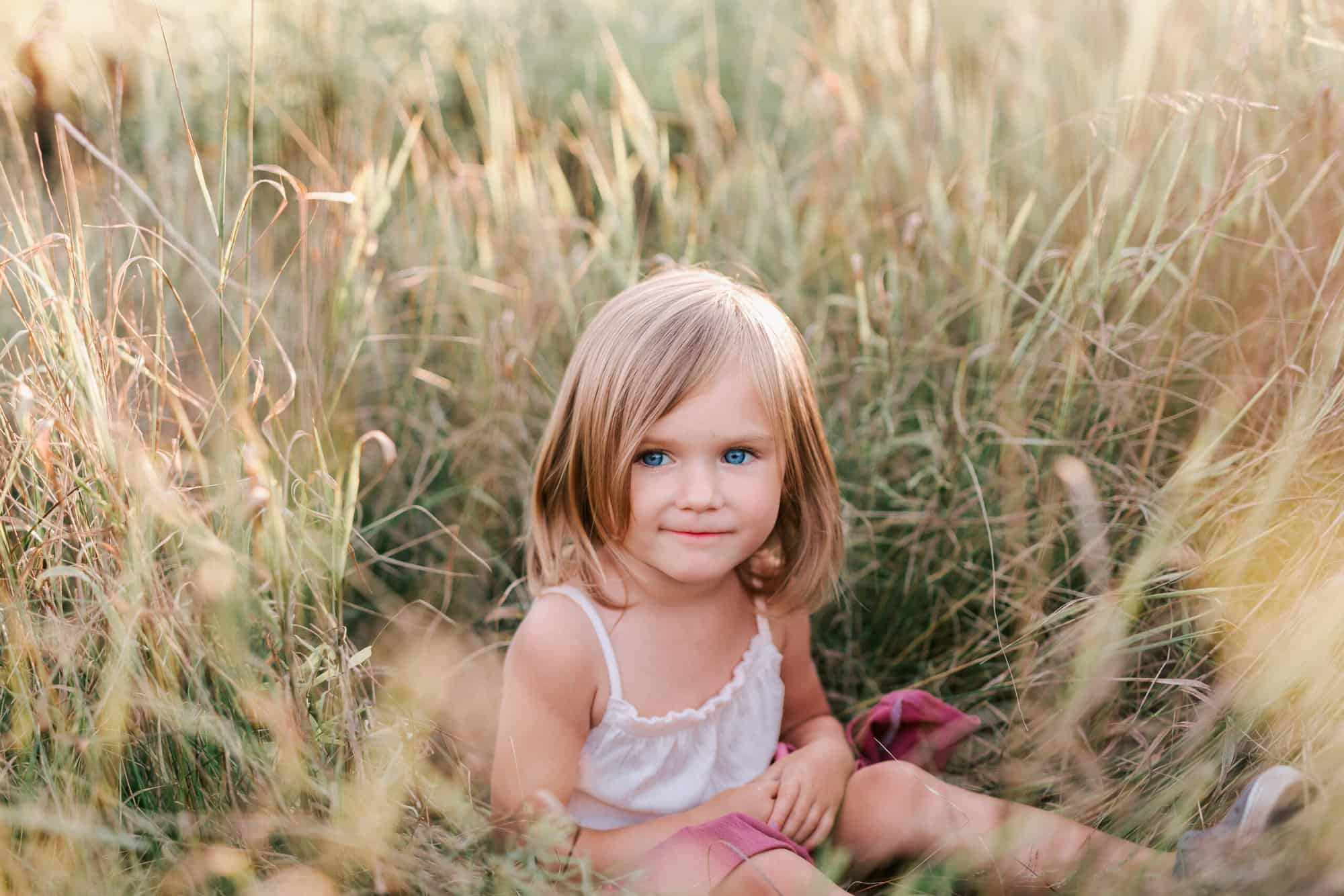 Little girl in a dress sitting in a grassy field from The Sharing Squirrel by Chelsey Kae Photography